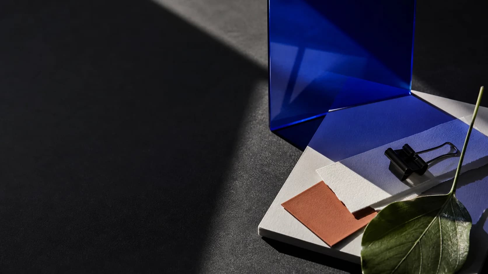 Blue acrylic panels, paper swatches, and a binder clip arranged as a campaign direction study. Synthetic sample.