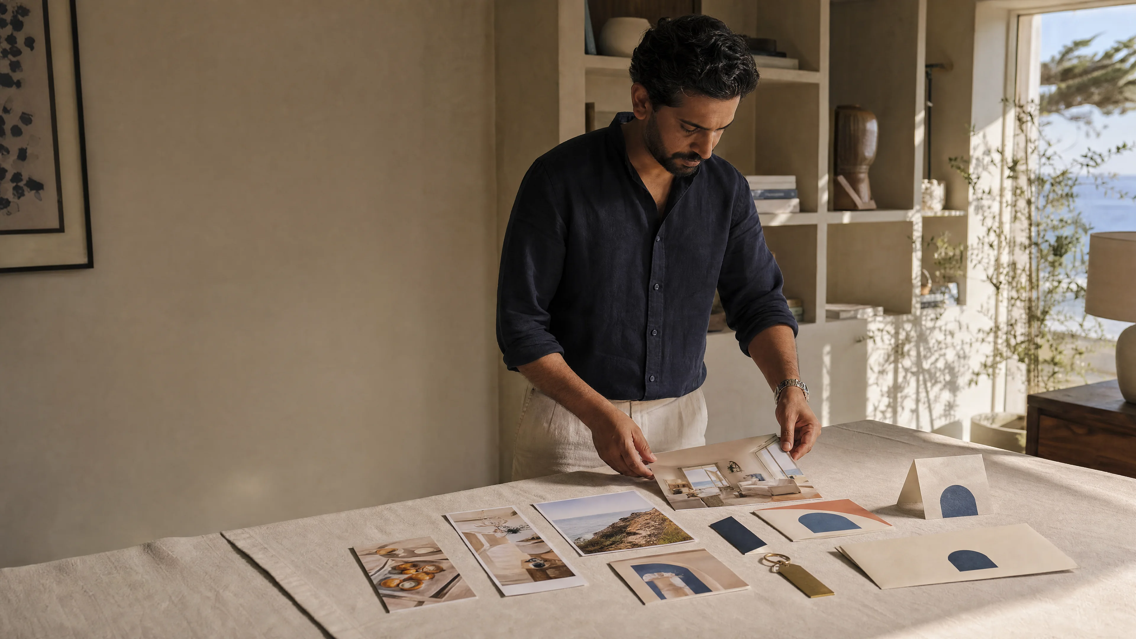 A person laying out printed hospitality brand boards for a client campaign on a linen table. Synthetic sample.